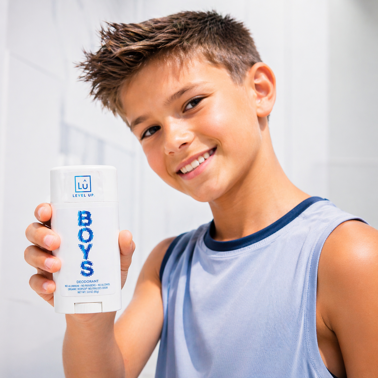 Young boy holding a 'BOYS' deodorant container against a plain background